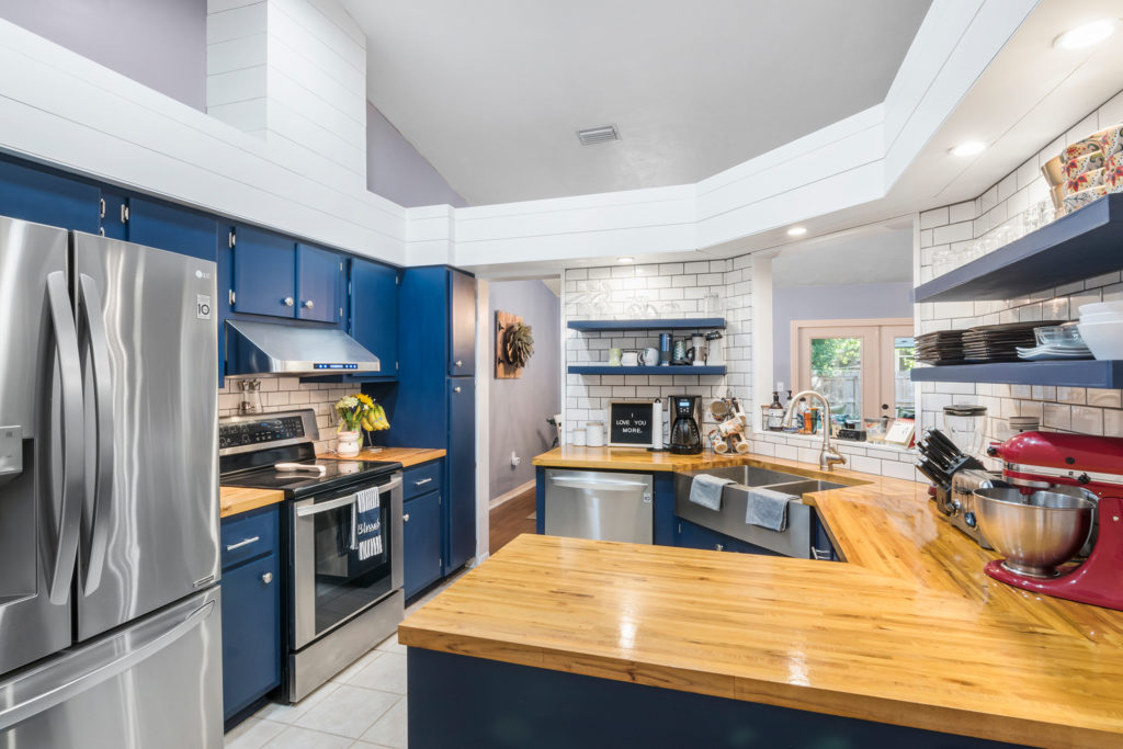 Modern kitchen with blue cabinetry, stainless steel appliances, and a central wooden island.